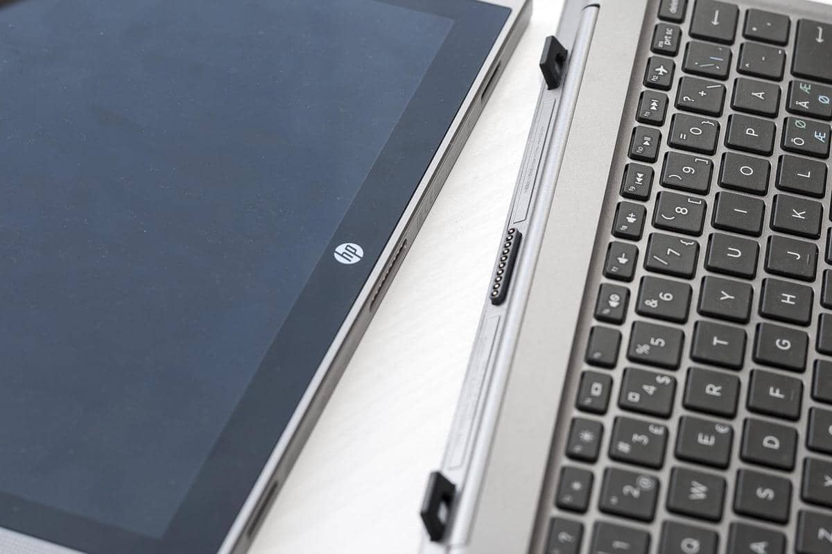 Laptop HP EliteBook berwarna perak dengan layar terlepas dari keyboard, menampilkan desain ramping dan modern di atas meja putih.