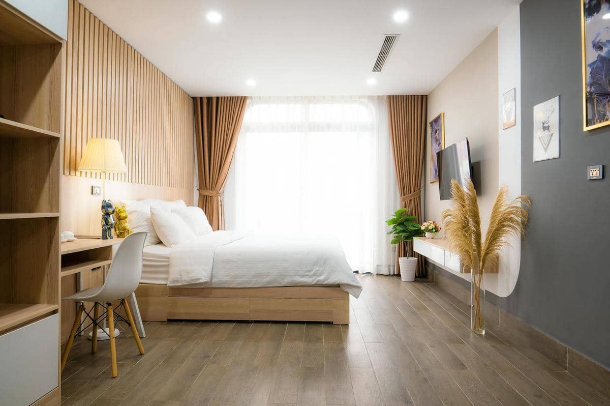 Kamar tidur modern dengan desain minimalis, dinding kayu vertikal, tempat tidur putih, dan pencahayaan alami dari jendela besar.