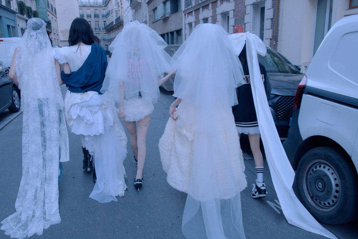 Lima orang berjalan di jalan kota dengan mengenakan busana unik berwarna putih dan biru, beberapa memakai veil panjang seperti gaun pengantin.