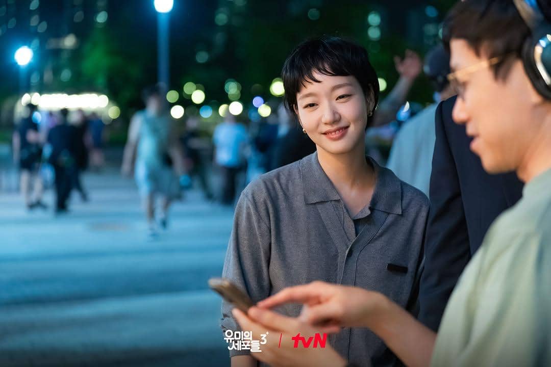 Seorang aktris tersenyum sambil melihat layar ponsel bersama kru di lokasi syuting malam hari untuk serial Yumi's Cells 3.