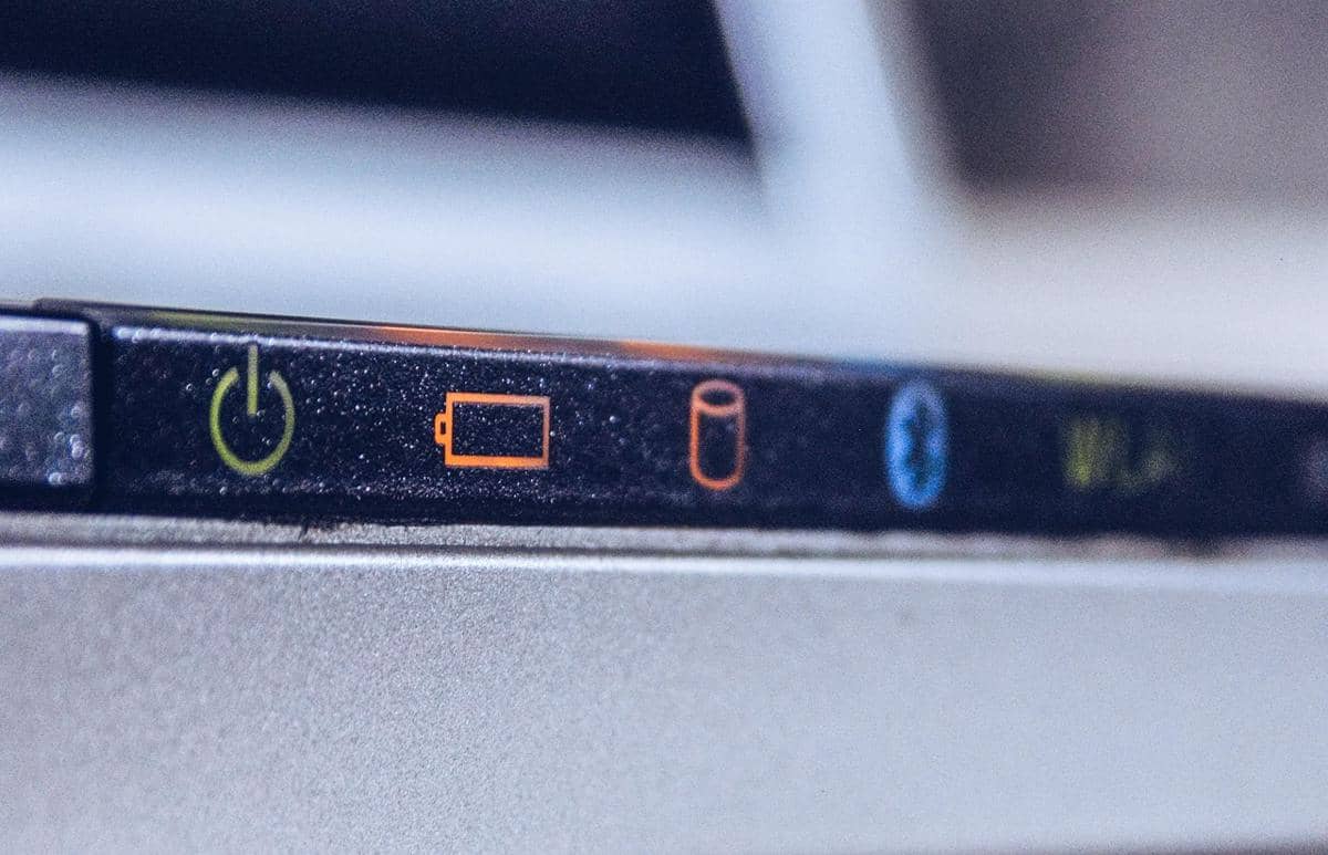 Tombol daya dan indikator baterai pada laptop dengan simbol berwarna hijau, oranye, dan biru terlihat di bagian tepi perangkat.