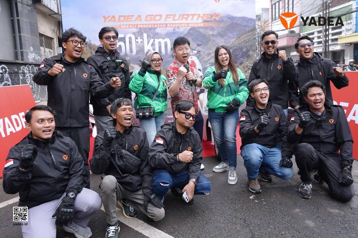 Sekelompok orang berpose bersama di acara Yadea Go Further dengan latar spanduk bertema perjalanan Bandung-Bogor sejauh 150 km.