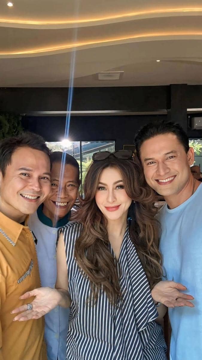 Empat orang berdiri berdekatan sambil tersenyum di dalam ruangan dengan pencahayaan hangat, tampak akrab dan bahagia.