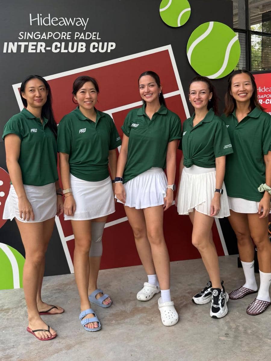 Lima wanita mengenakan seragam hijau dan rok putih berpose bersama di depan papan bertuliskan Singapore Padel Inter-Club Cup.