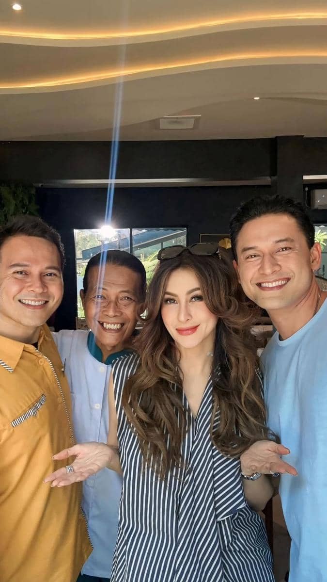 Empat orang berdiri berdekatan sambil tersenyum di dalam ruangan dengan pencahayaan alami dari jendela di belakang mereka.