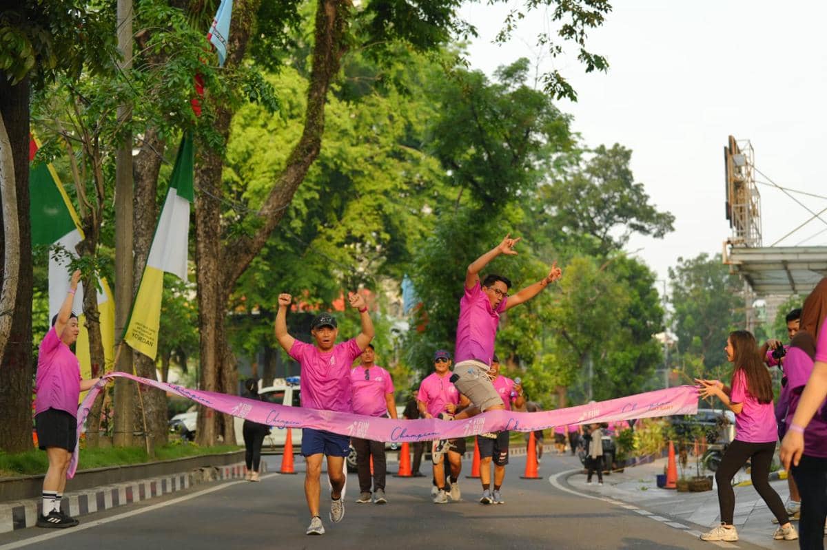 Peserta Fun Walk 5K Aryaduta Medan mengenakan kaus ungu melintasi garis finis dengan semangat di jalan yang rindang.