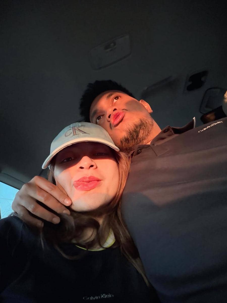 Nathalie Holscher dan Arifat berpose bersama di dalam mobil dengan cahaya matahari sore menyinari wajah mereka.