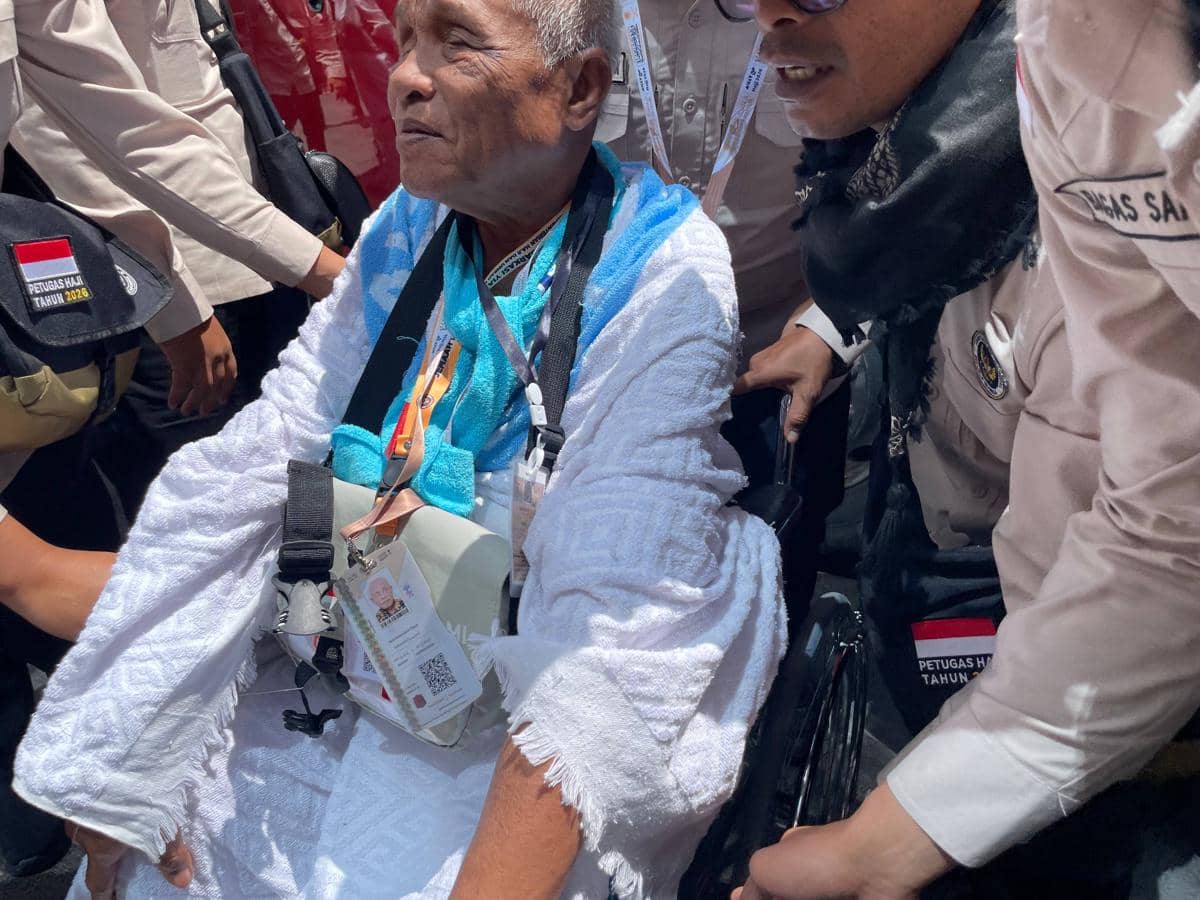 Seorang jemaah lanjut usia mengenakan kain ihram duduk di kursi roda, didampingi petugas haji yang mengenakan seragam krem di Makkah.