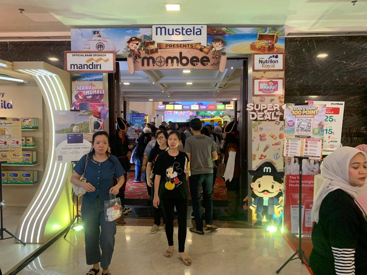Pengunjung berjalan di area masuk Mombee Expo 2026 di Medan dengan berbagai stan sponsor dan dekorasi bertema keluarga.