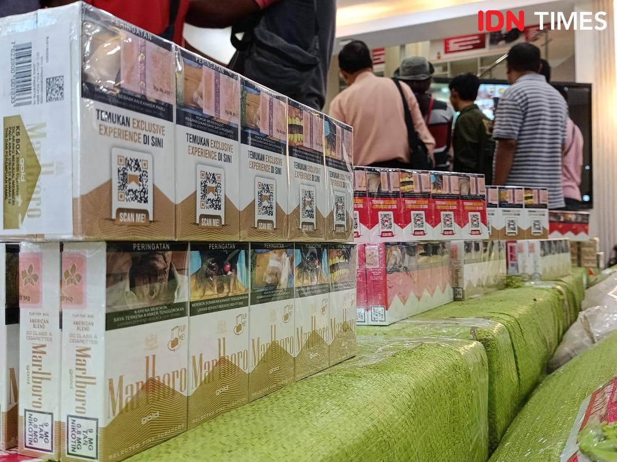 Tumpukan bungkus rokok merek Marlboro palsu yang disita oleh Polda NTT dan Bea Cukai di Belu, dengan beberapa orang berdiri di latar belakang.