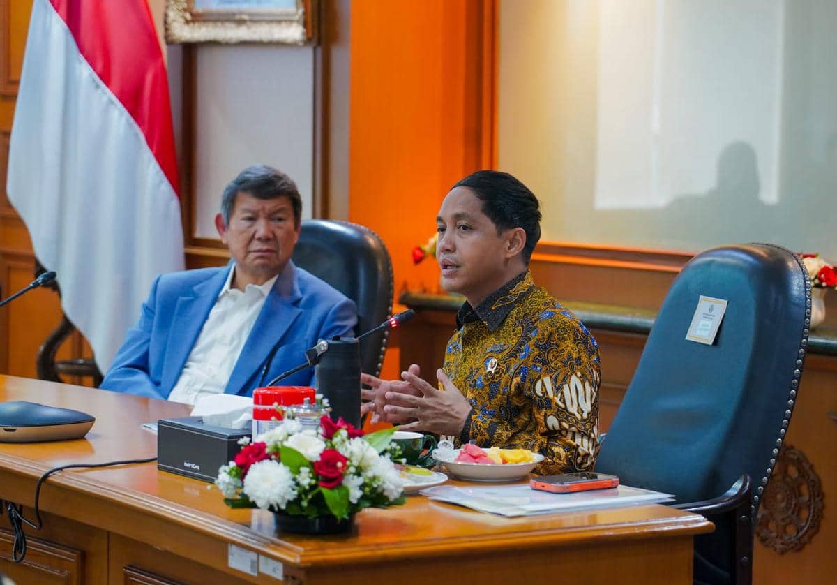 Dua pejabat Kemenhut berbincang dalam pertemuan bersama NGO di ruang rapat dengan latar bendera Indonesia dan meja berisi dokumen serta bunga.
