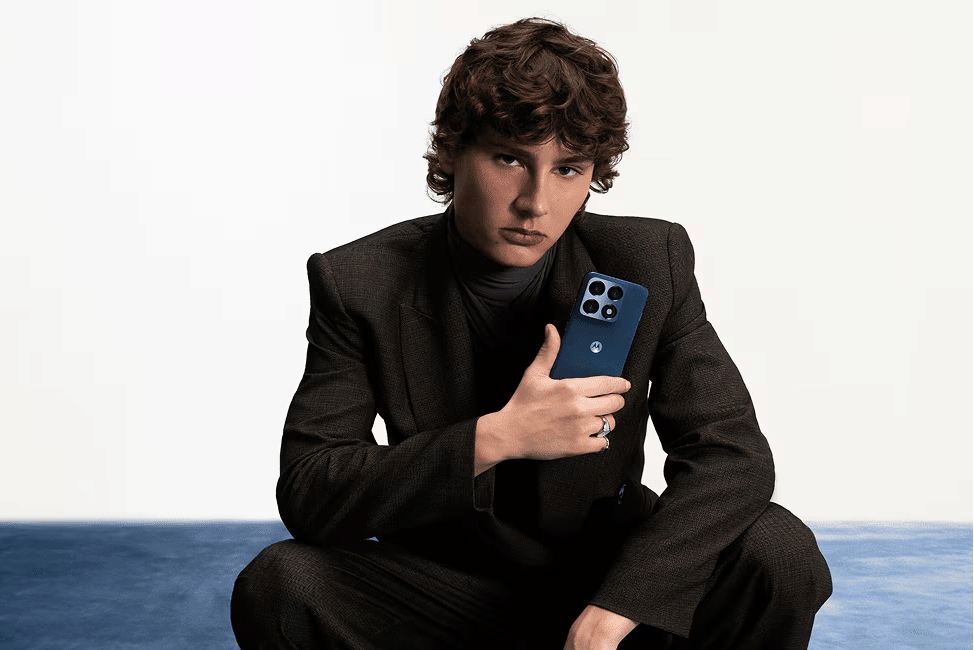 Seorang pria mengenakan setelan gelap memegang ponsel Motorola Edge 70 Pro berwarna biru dengan empat kamera belakang.