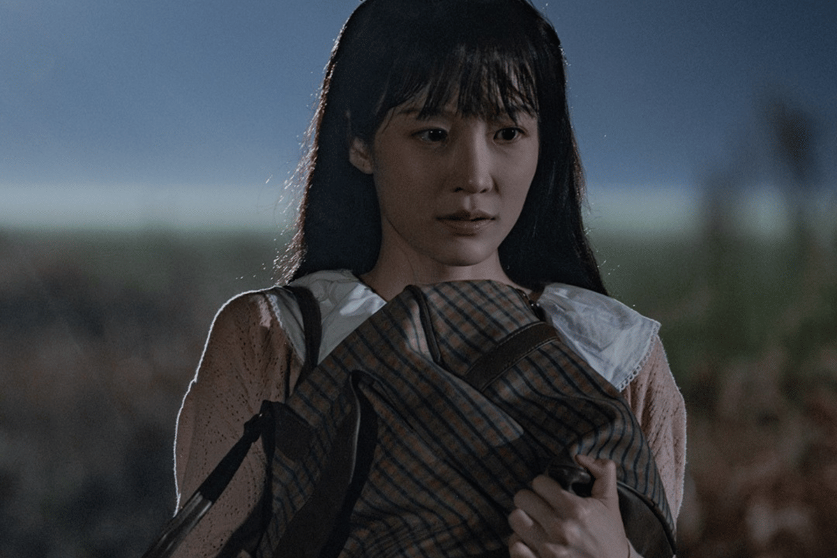 Seorang perempuan berambut panjang memeluk tas di tengah suasana malam dengan latar belakang kabur dalam adegan drama The Scarecrow.