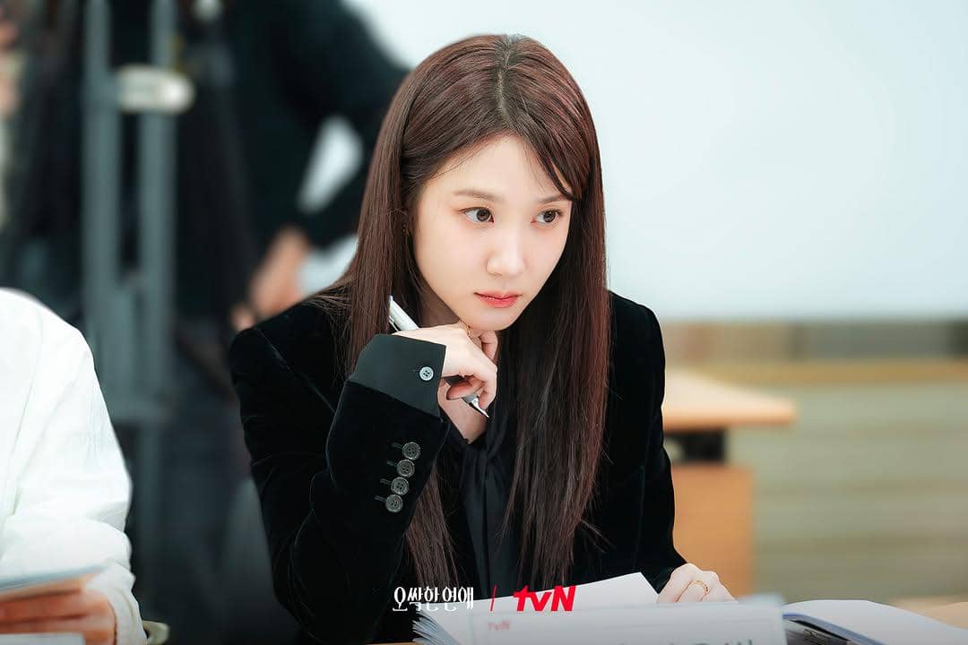 Seorang aktris mengenakan blazer hitam sedang fokus membaca naskah di meja dalam sesi pembacaan naskah drama Spooky in Love.