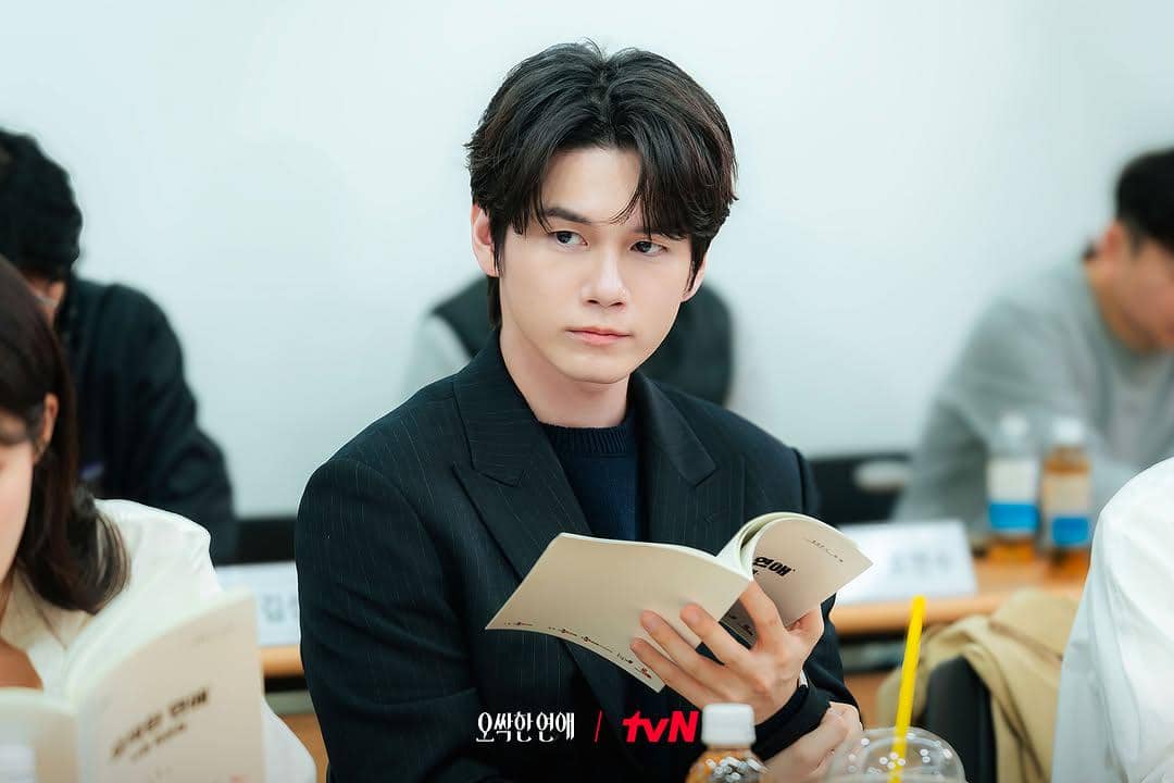 Seorang aktor mengenakan setelan hitam sedang membaca naskah di meja selama sesi pembacaan naskah drama Spooky in Love.