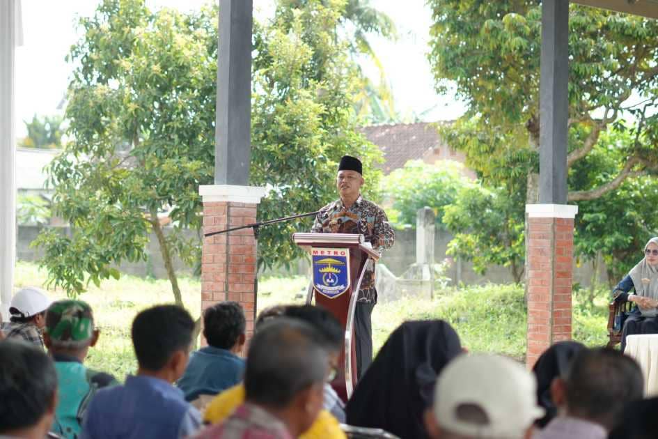 Seorang pejabat berbicara di podium bertuliskan Metro saat dialog Pemkot Metro dengan kelompok tani di area pertanian terbuka.