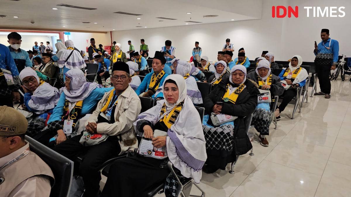 Calon jemaah haji asal Tangerang duduk di ruang tunggu dengan mengenakan pakaian ihram dan atribut haji berwarna kuning hitam.
