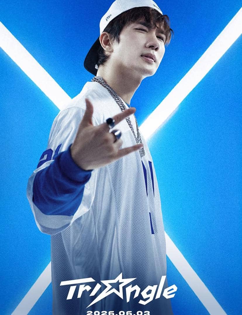 Seorang pria mengenakan topi putih terbalik dan jersey biru putih berpose dengan latar belakang biru bercahaya berbentuk silang.