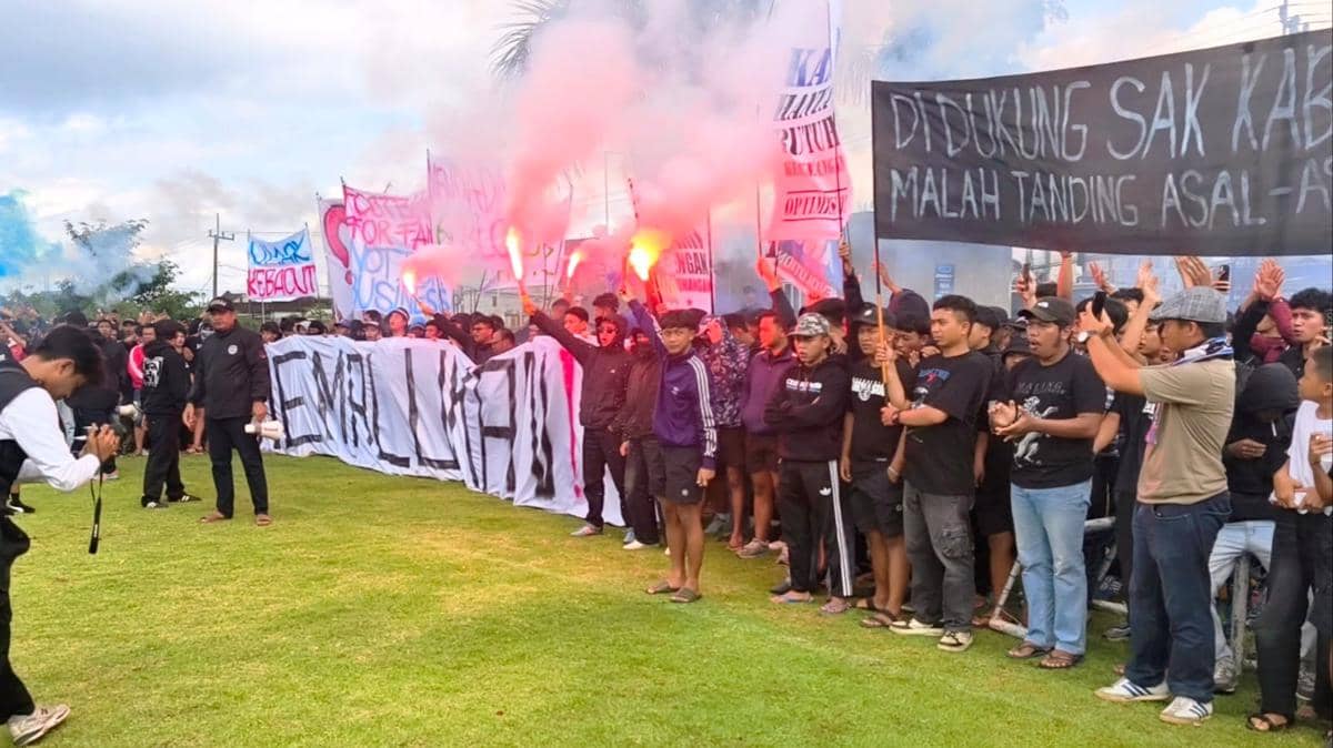 Sejumlah Aremania melakukan demonstrasi di Lapangan DFP, Kabupaten Malang, sambil membawa spanduk dan menyalakan flare berwarna merah.