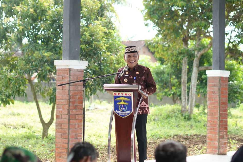 Seorang pejabat Pemkot Metro berbicara di podium bertanda Metro saat dialog dengan kelompok tani di area pertanian terbuka.