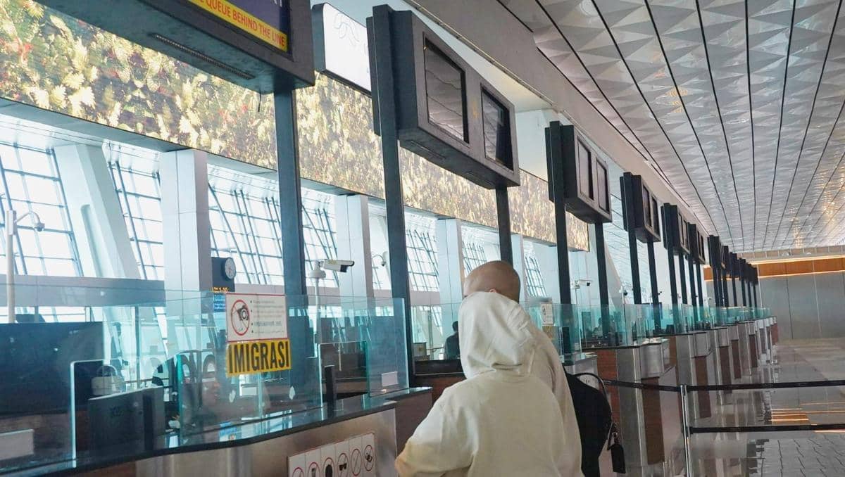 Penumpang mengenakan pakaian terang sedang melintasi area pemeriksaan imigrasi di Bandara Soekarno-Hatta dengan deretan loket kosong.