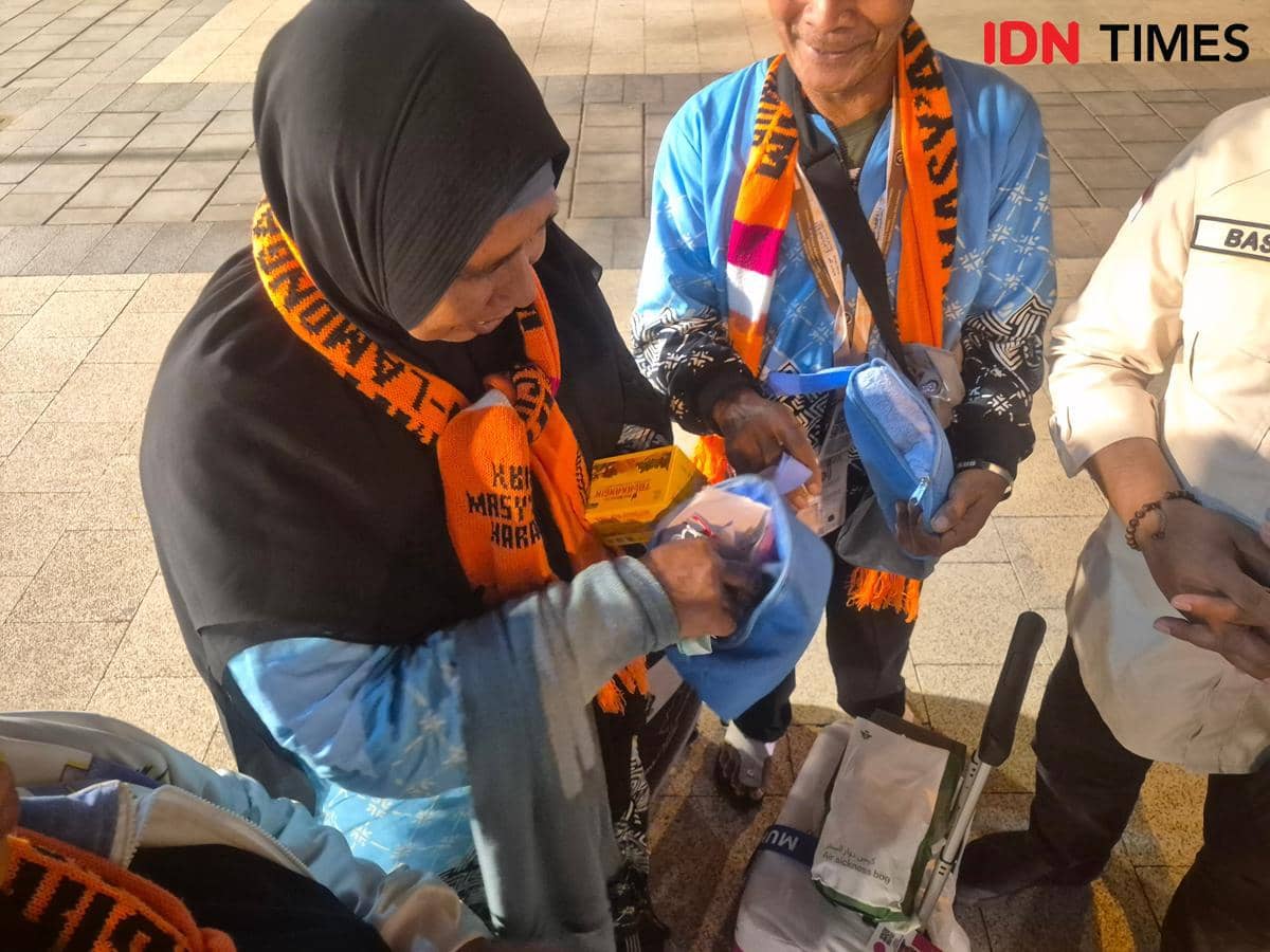 Jemaah haji Kloter 32 asal Embarkasi Surabaya mengenakan syal oranye dan memegang travel kit berwarna biru pemberian pemerintah.
