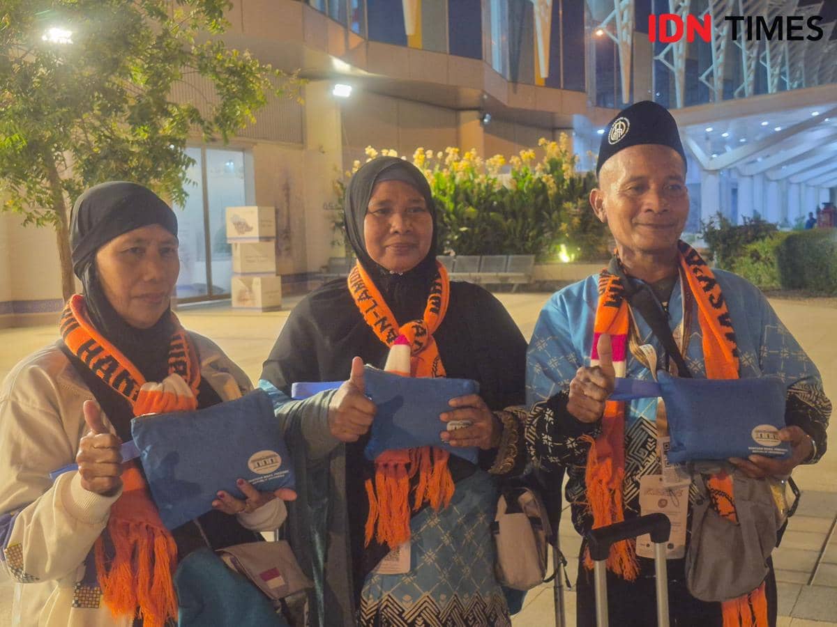 Tiga jemaah haji Kloter 32 Embarkasi Surabaya memegang travel kit berwarna biru dari Pemerintah Indonesia sambil berpose bersama.