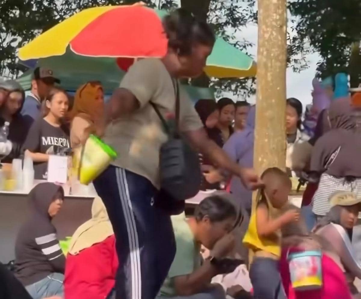 Seorang perempuan menarik anak kecil di area ramai dekat Stadion Kanjuruhan, dikelilingi orang-orang dan pedagang di bawah payung warna-warni.