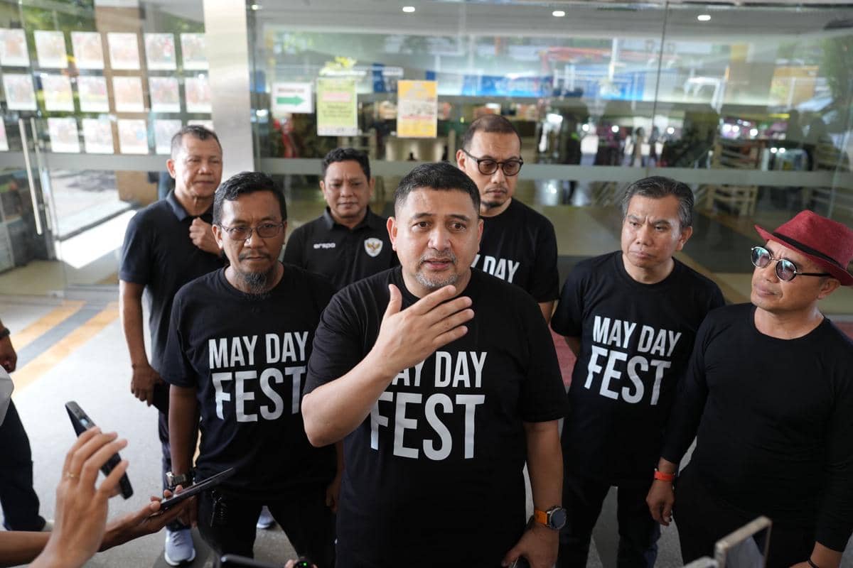 Seorang pria berbicara kepada media didampingi beberapa orang mengenakan kaus hitam bertuliskan May Day Fest di Makassar.