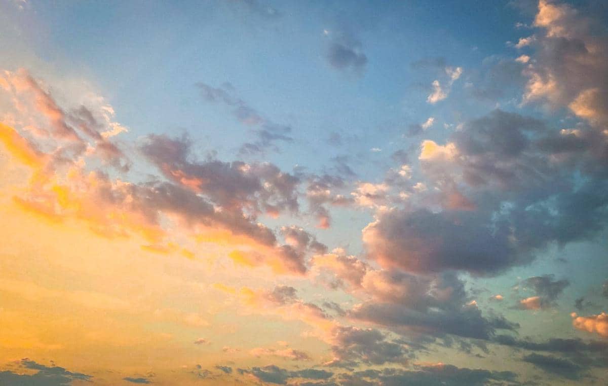 Langit berwarna biru dan oranye dengan awan lembut saat matahari terbenam, menggambarkan suasana atmosfer yang tenang.