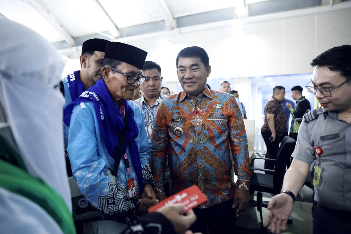 Seorang pejabat Sulawesi Utara mengenakan batik berwarna biru-oranye berbincang dengan jamaah calon haji di Bandara Sam Ratulangi Manado.