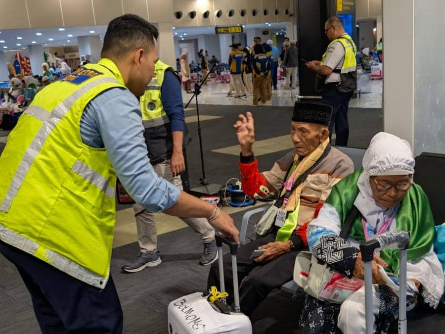 Petugas bandara berbicara dengan dua calon jemaah haji lanjut usia yang duduk di kursi tunggu Bandara Sam Ratulangi Manado.