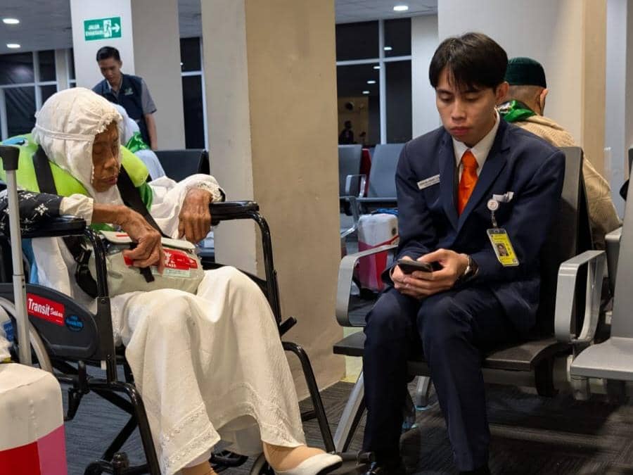 Jemaah calon haji lanjut usia duduk di kursi roda didampingi petugas bandara di ruang tunggu Bandara Sam Ratulangi Manado.