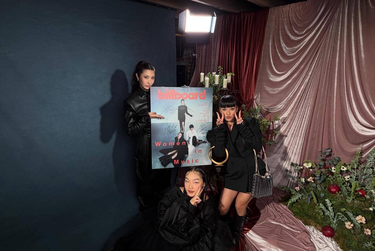Ejae, Rei Ami, Audrey Nuna berpose bersama poster Billboard Women in Music 2026 di latar dekorasi elegan dengan kain beludru dan bunga.