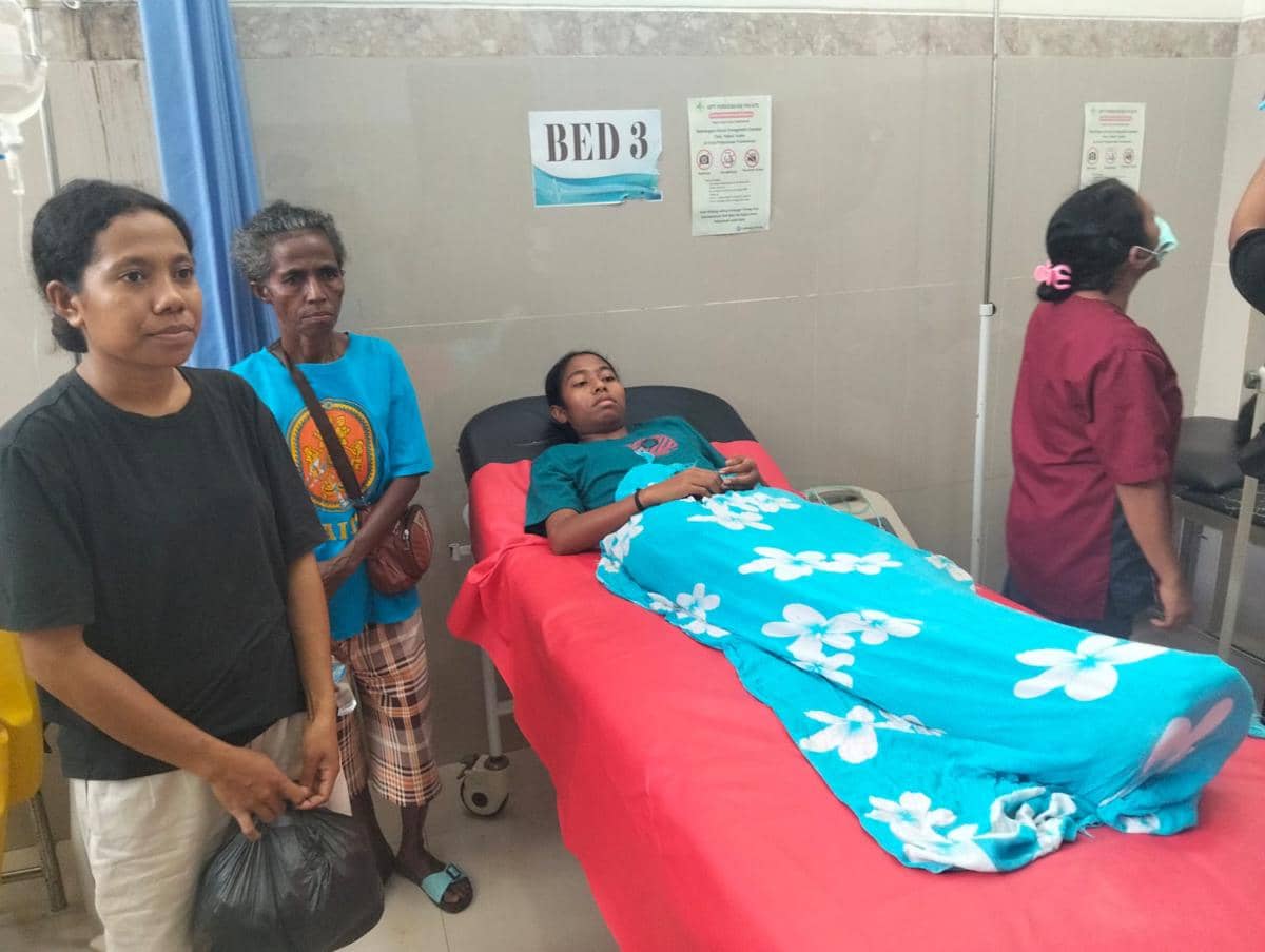 Seorang pasien perempuan terbaring di ranjang rumah sakit dengan selimut biru bermotif bunga, didampingi keluarga dan tenaga medis di Amanuban, TTS.