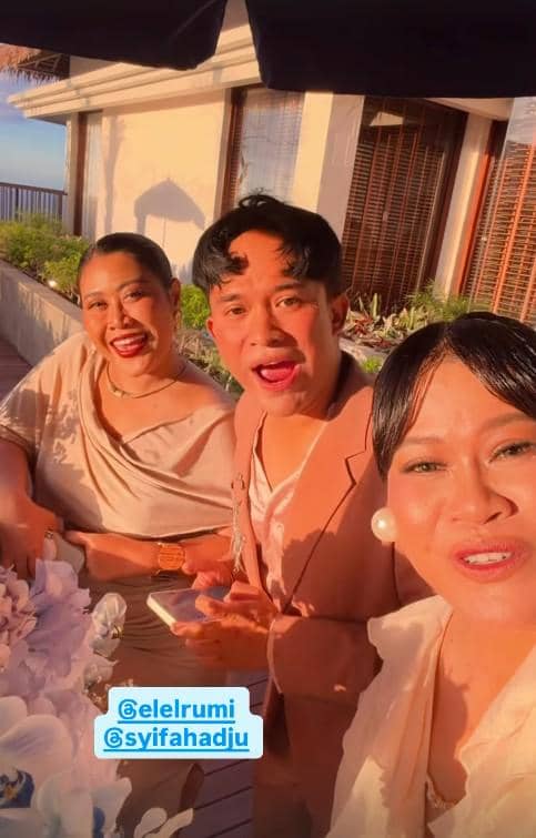 Tiga tamu berpakaian formal berpose ceria di acara resepsi pernikahan yang berlangsung di Bali dengan latar suasana senja.