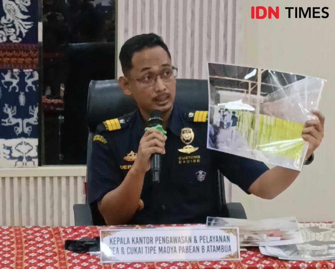 Seorang pejabat Bea dan Cukai Atambua mengenakan seragam dinas sedang memegang mikrofon dan memperlihatkan foto saat konferensi pers.