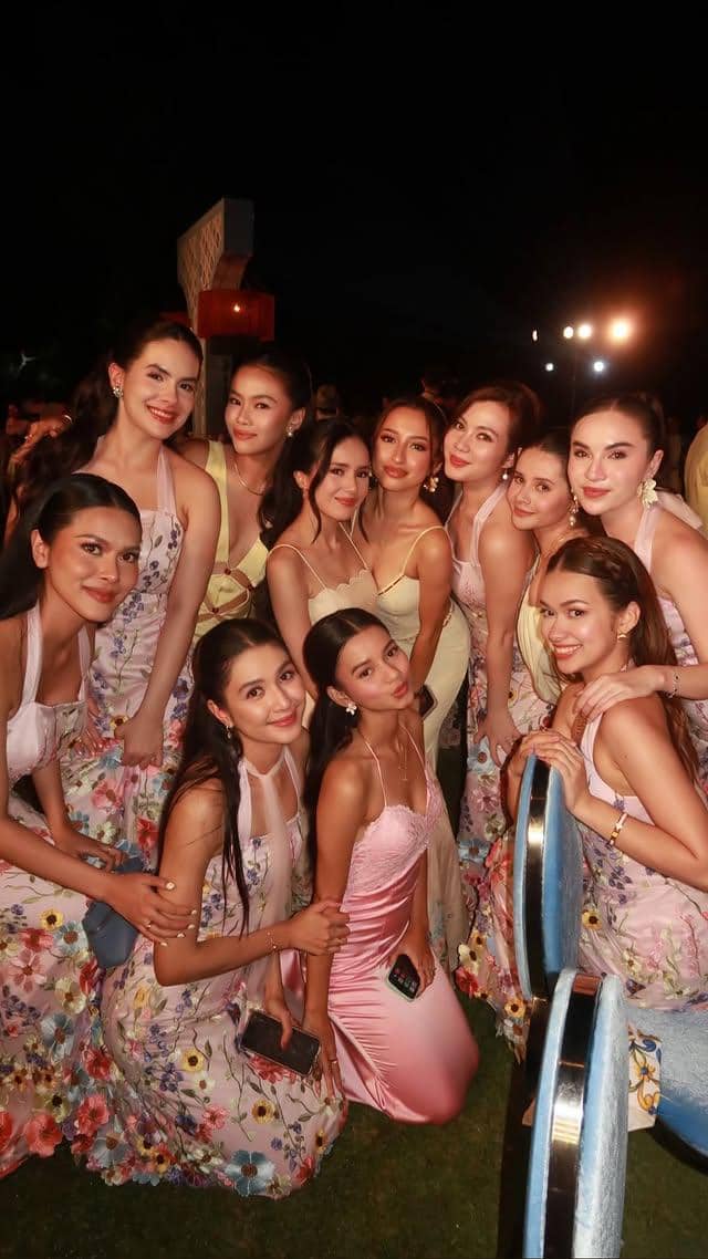 Sekelompok bridesmaid berpose bersama di malam hari mengenakan gaun berwarna pastel dan bermotif bunga dalam suasana pesta pernikahan.