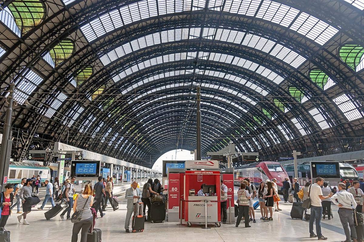 Pemandangan aula utama di dalam stasiun kereta api Milano Centrale di Italia, yang menampilkan atap lengkung besar dari logam dan kaca yang khas.