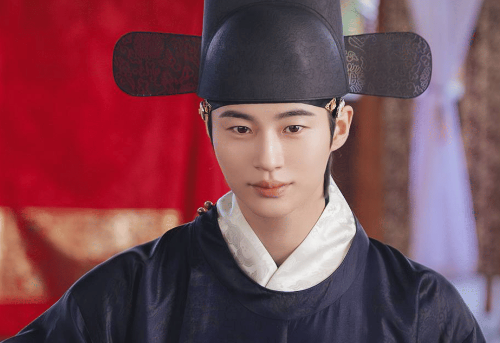 Aktor mengenakan hanbok kerajaan berwarna gelap dan topi tradisional Korea dalam cuplikan drama Korea Perfect Crown.