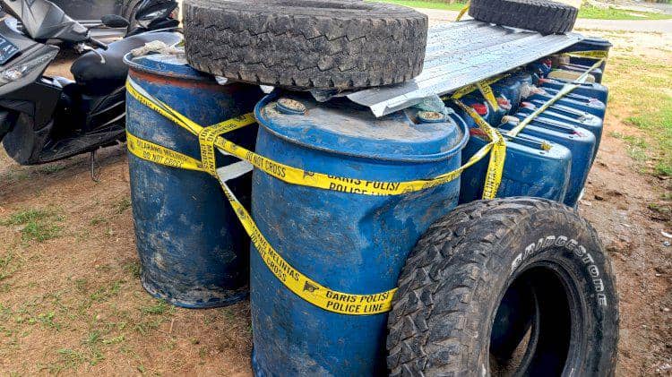 Deretan drum biru berisi BBM solar disegel dengan garis polisi di Rote, bersama ban mobil dan jeriken di sekitarnya.