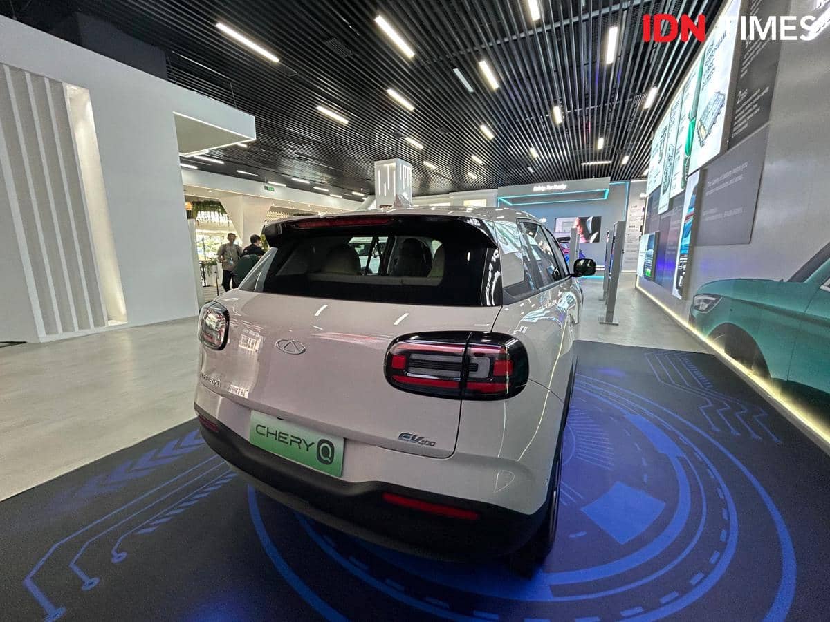Tampak belakang mobil Chery Q berwarna putih dengan desain buritan membulat dipamerkan di ruang pamer modern berlampu neon.