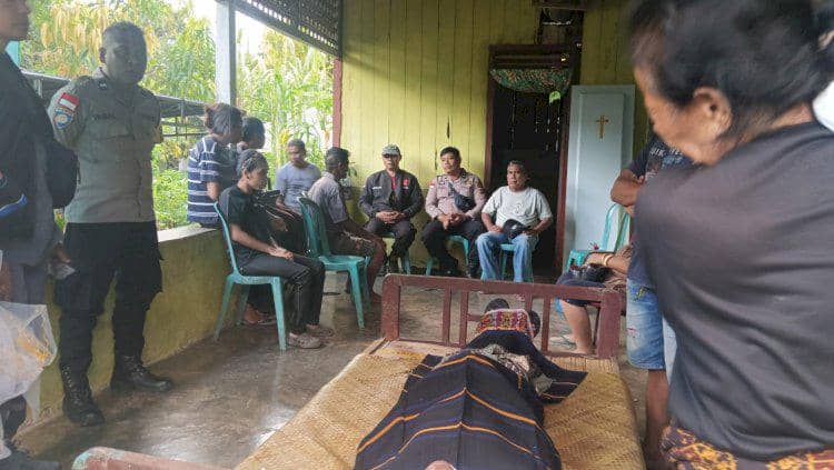 Beberapa orang duduk dan berdiri di rumah duka di Sikka, dengan jenazah petani terbaring di atas tikar dan peti kayu sederhana.