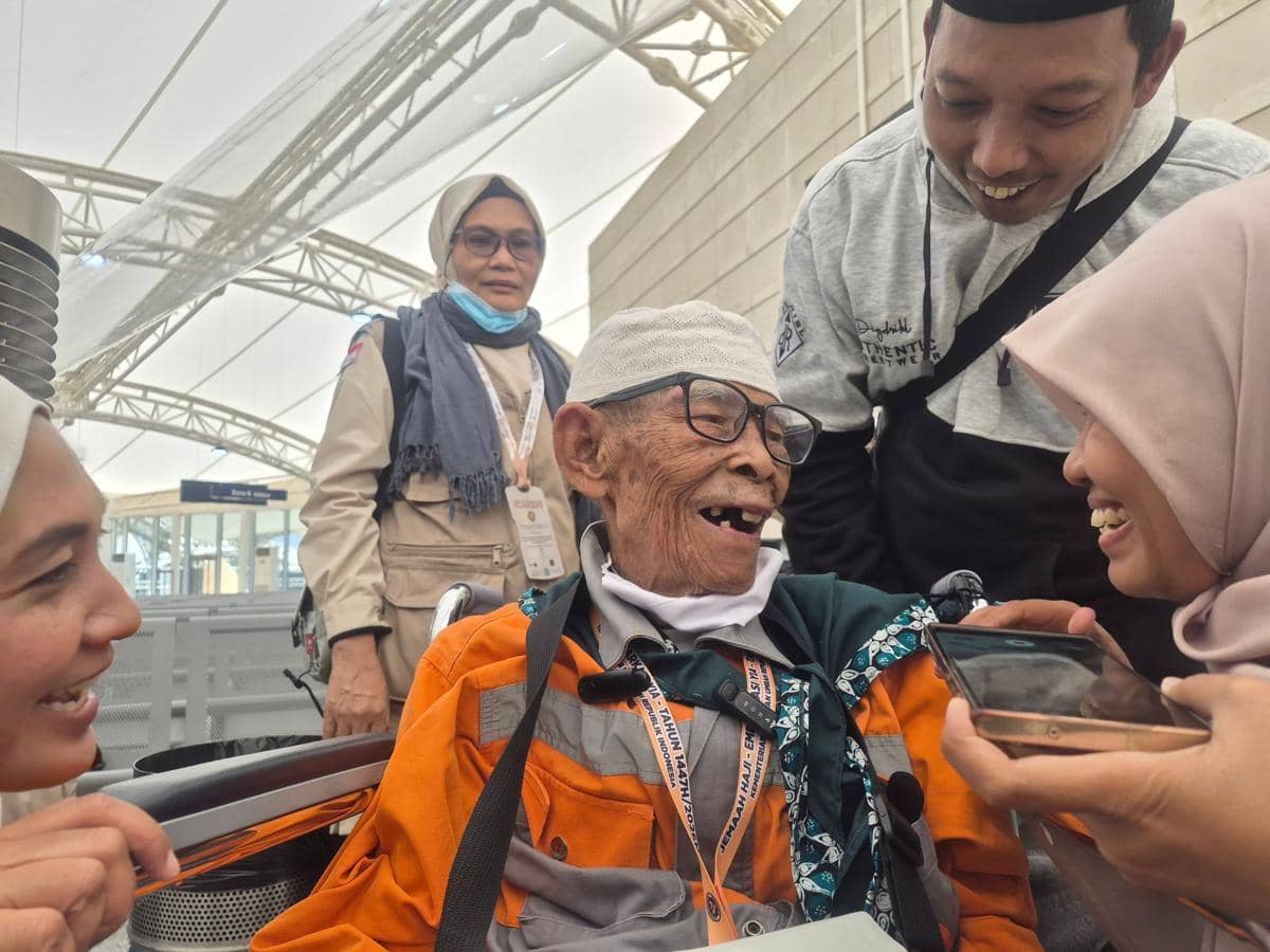 Seorang jemaah haji lanjut usia tersenyum bahagia sambil berbincang dengan para pendamping di Bandara Internasional Madinah.