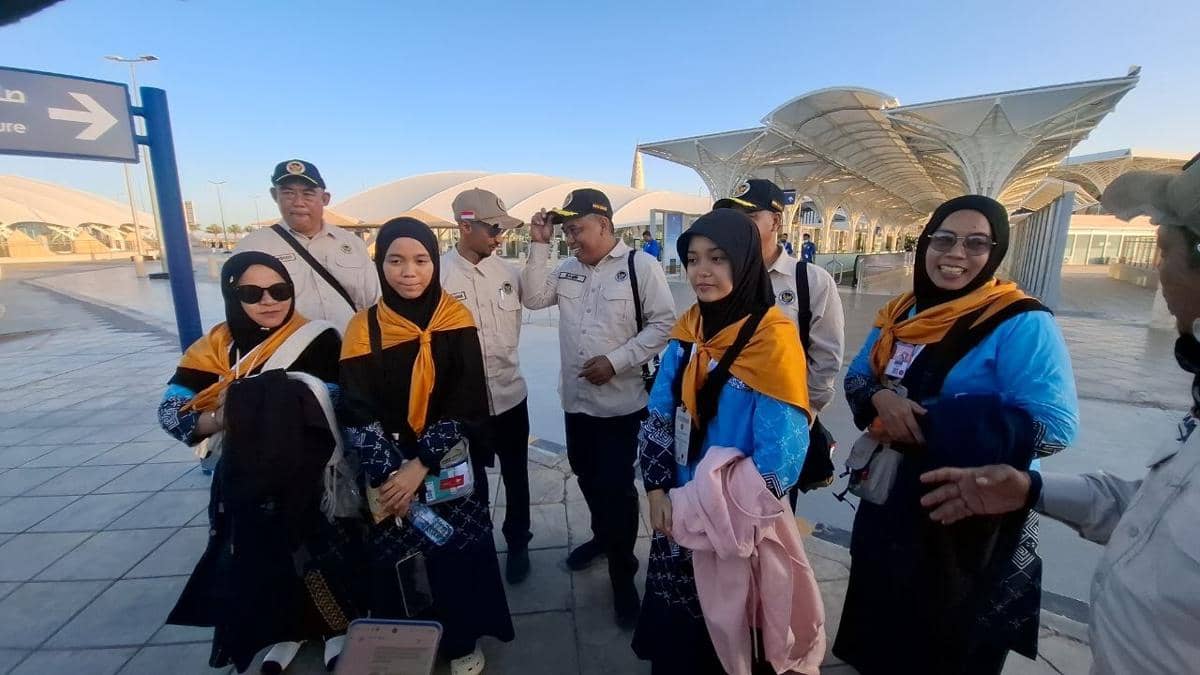 Sejumlah petugas PPIH dan jemaah haji mengenakan seragam biru dan rompi oranye berfoto bersama di area luar Bandara Prince Mohammad bin Abdul Aziz.