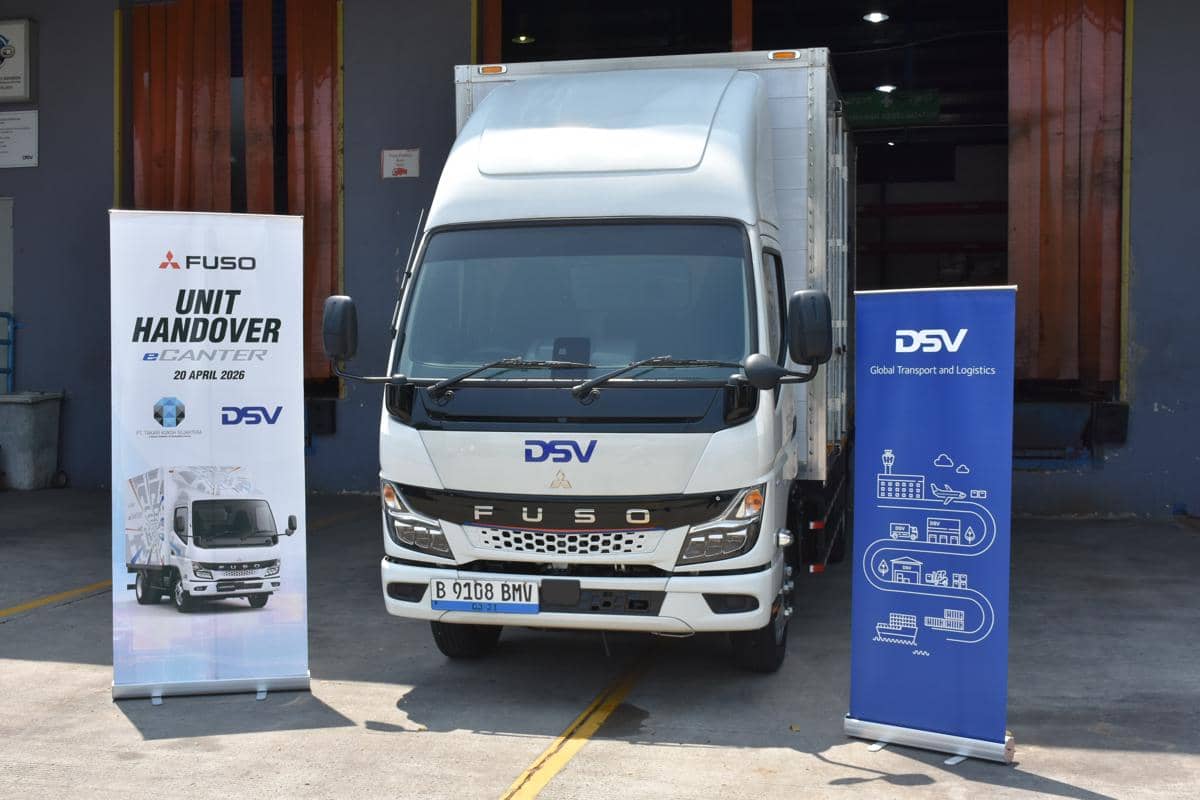 Truk listrik Mitsubishi Fuso eCanter berwarna putih dengan logo DSV diparkir di depan gudang bersama dua banner acara serah terima unit.