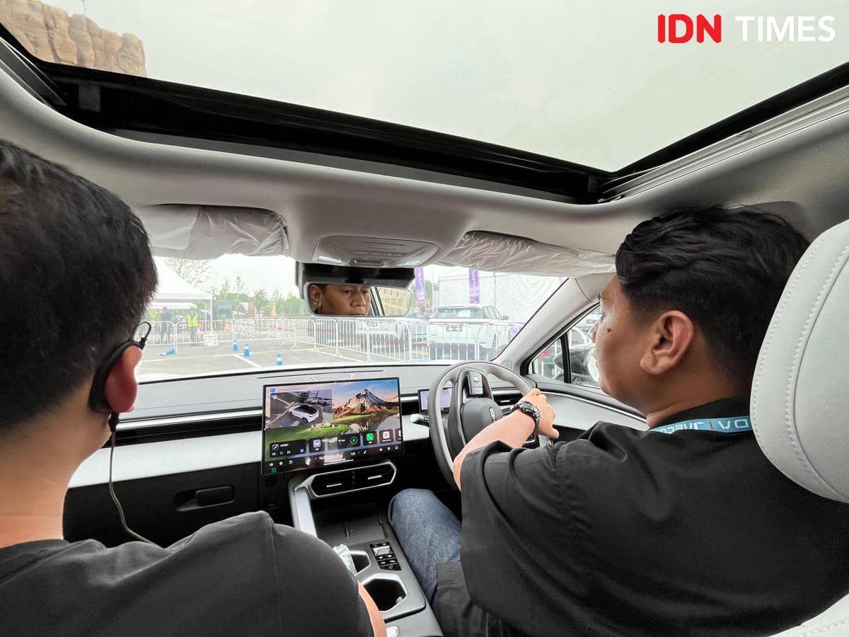 Dua orang berada di dalam mobil listrik Chery E5 EV facelift, salah satunya sedang mengemudi dengan layar digital besar di dashboard.