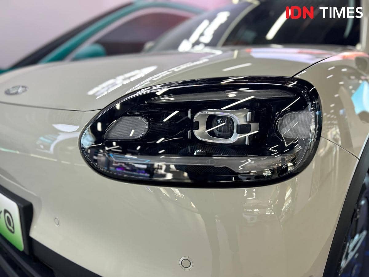 Tampilan dekat lampu utama mobil Chery Q dengan desain modern dan refleksi pencahayaan di permukaan bodi berwarna krem.