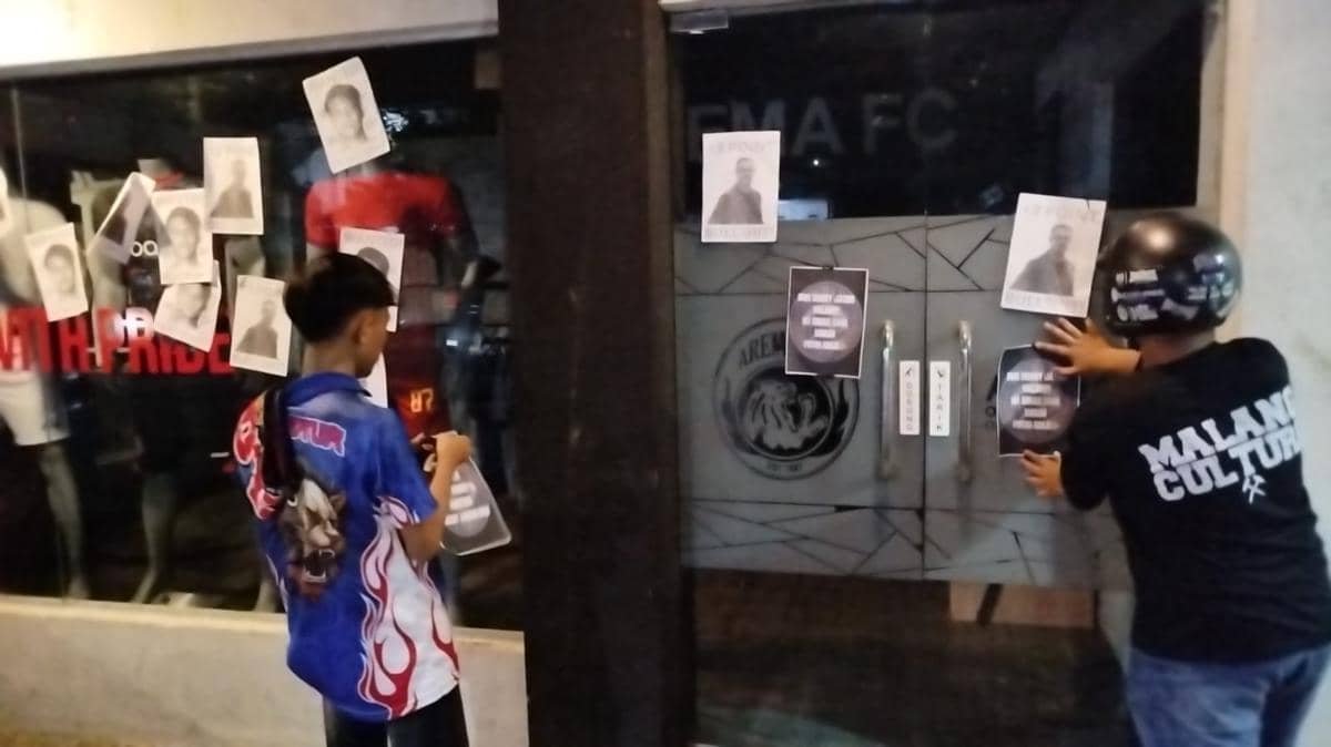 Dua orang Aremania menempelkan poster di pintu kantor Arema FC setelah kekalahan tim dari Persik Kediri pada malam hari.