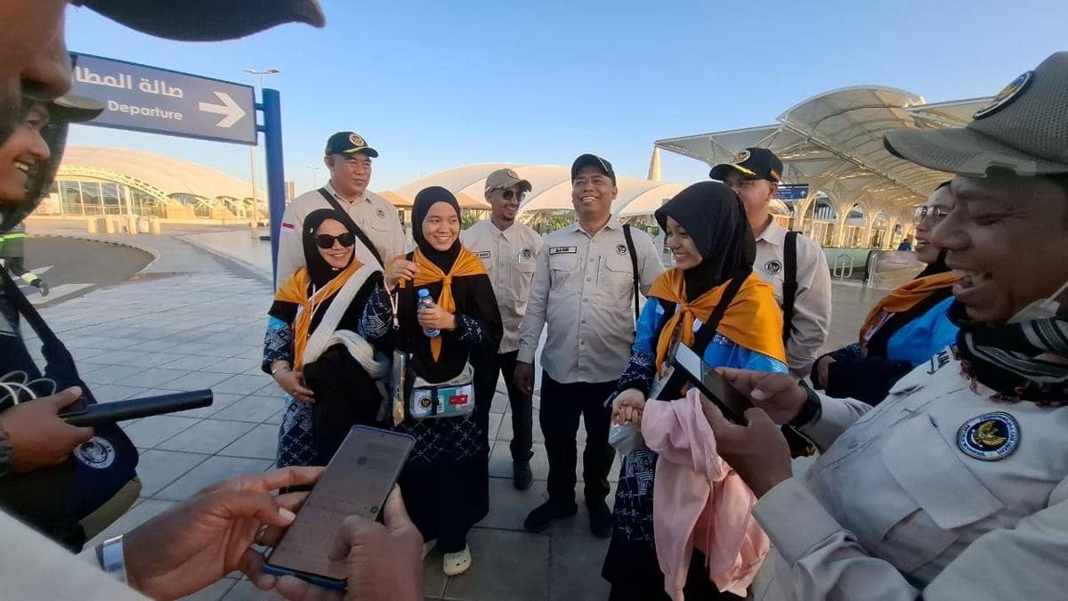 Sejumlah petugas PPIH dan jemaah haji mengenakan seragam serta syal oranye berbincang dan tersenyum di area bandara Prince Mohammad bin Abdul Aziz.